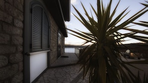 Un bâtiment en pierre doté d’un patio, d’une grande plante et offrant une vue sur une étendue d’eau.