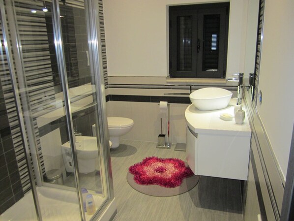 A modern bathroom with a glass-enclosed shower, a white sink with a bowl, and a toilet.