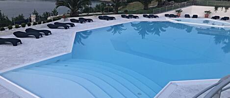 A swimming pool with lounge chairs and a view of hills and a body of water.