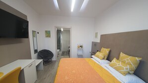 A modern hotel room with a bed, a desk, and a chair. There is a shower area visible through an open door. - Sunset Room - Room with double bed (Campolattaro)