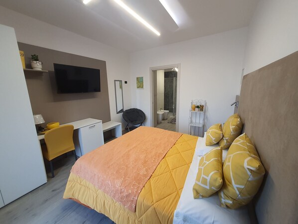 A hotel room with a bed, a desk, a chair, a TV, and a bathroom visible through an open door. - Sunset Room - Room with double bed (Campolattaro)