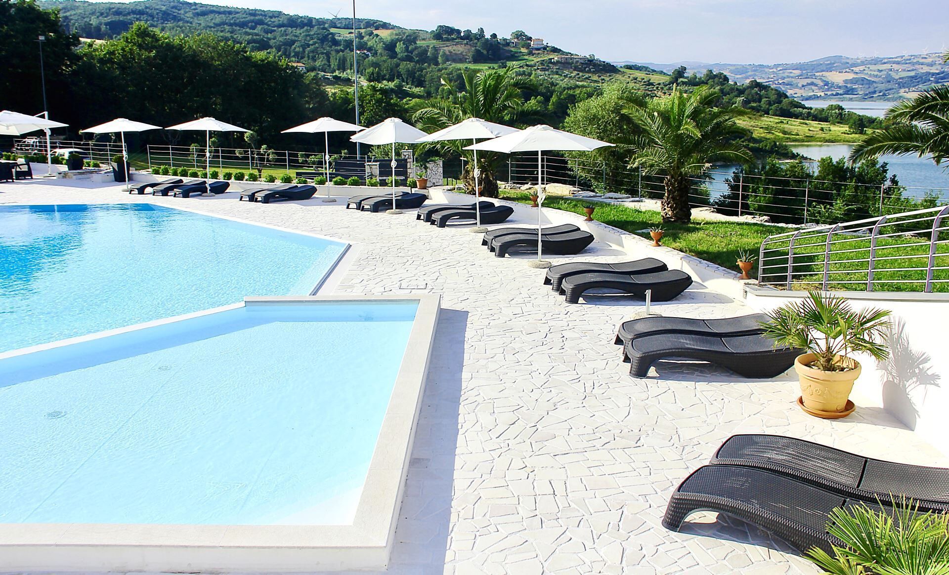 A swimming pool with lounge chairs and umbrellas, surrounded by greenery and a scenic view.