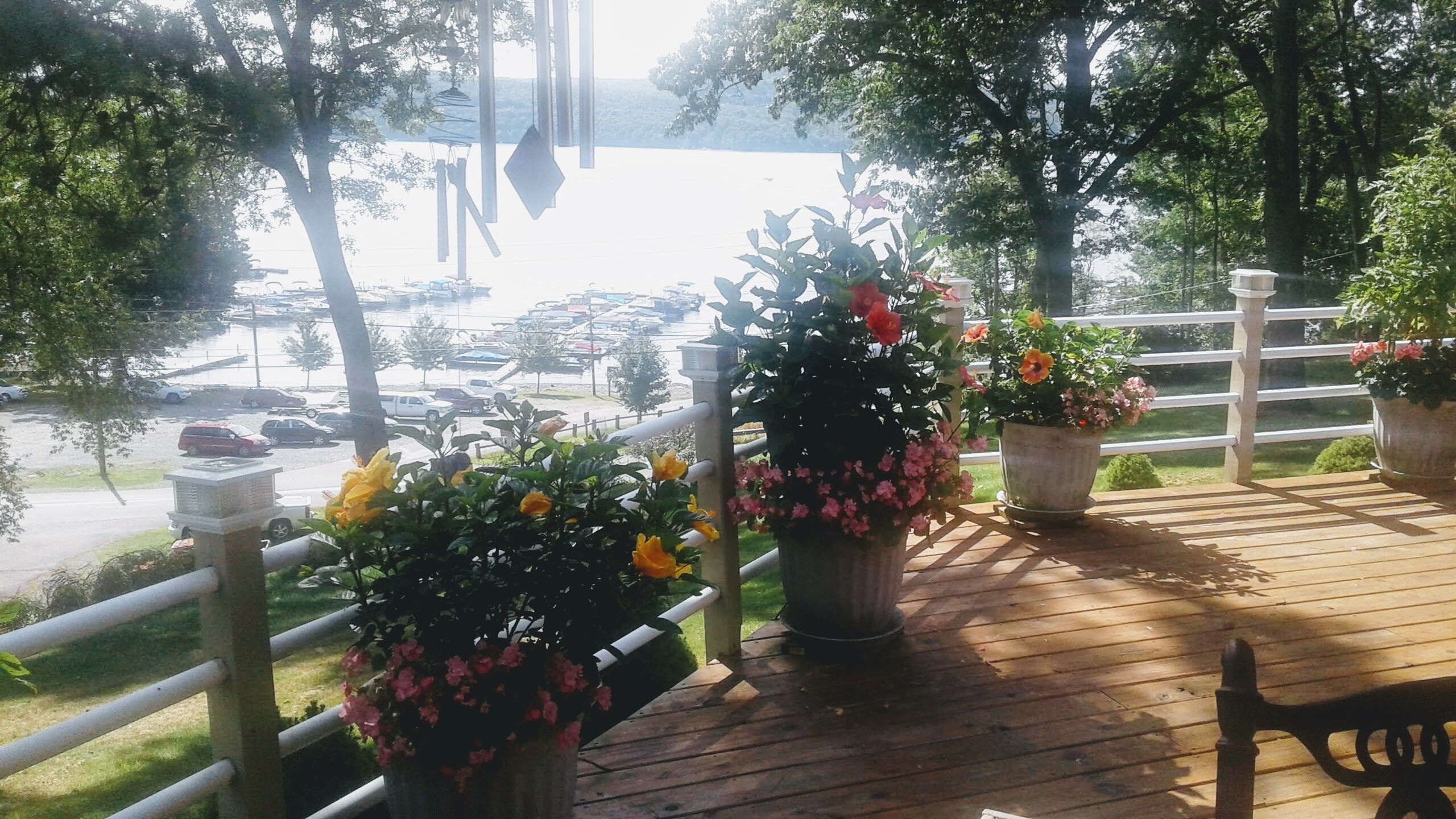 A wooden deck with potted plants and a view of a parking lot and water.