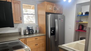 A compact kitchen with wooden cabinets, a stainless steel refrigerator, a built-in oven, and a window providing natural light. - Enjoy beautiful sunsets at a Lake Side Cottage (Tipton)