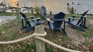 A lakeside deck with Adirondack chairs, a rope barrier, and a dock extending into the water. - Enjoy beautiful sunsets at a Lake Side Cottage (Tipton)