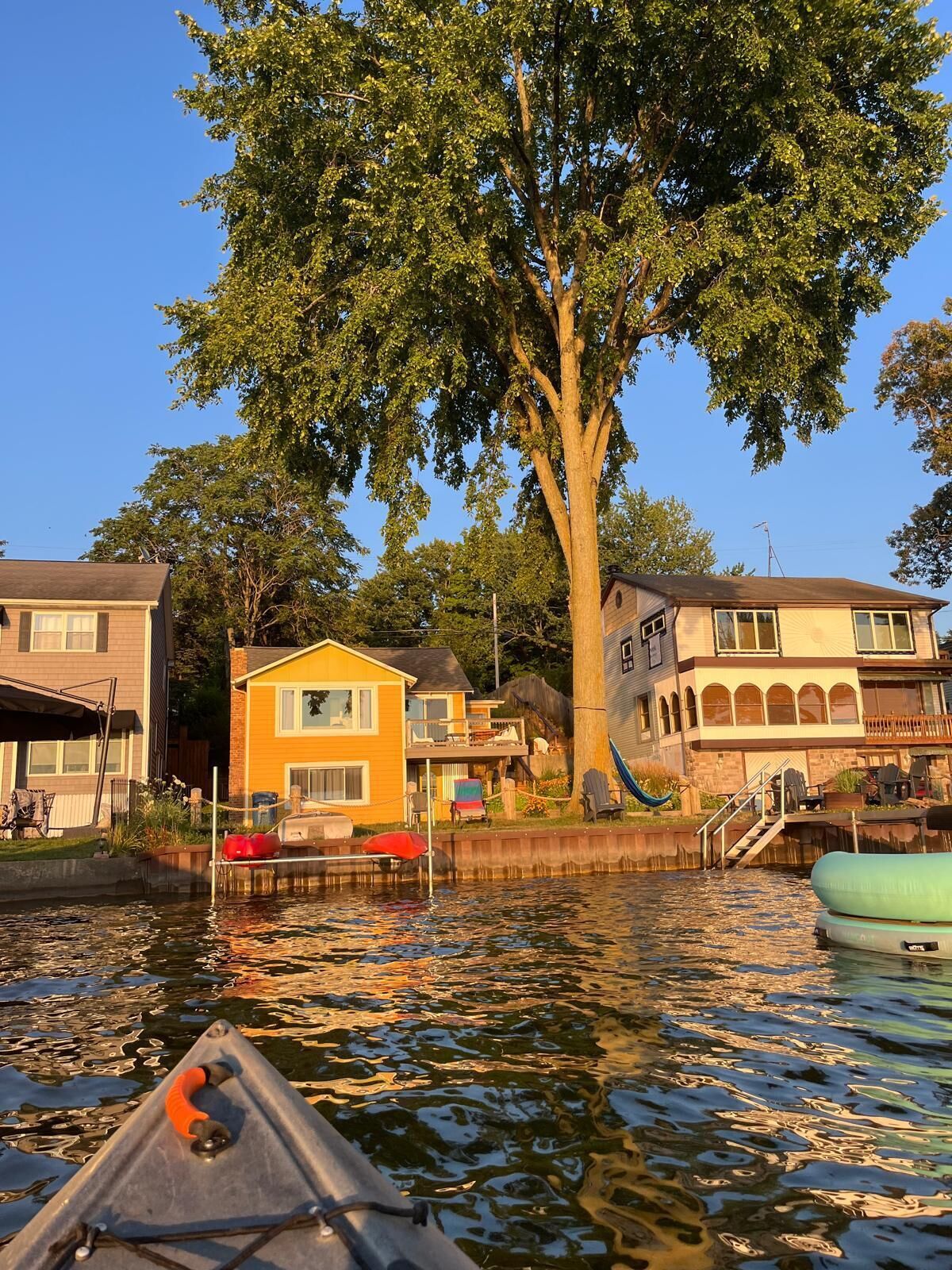 A houseboat docked near a tree-lined waterfront with a clear sky.