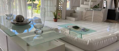 A modern living room with a glass coffee table, a white sofa, and a staircase.