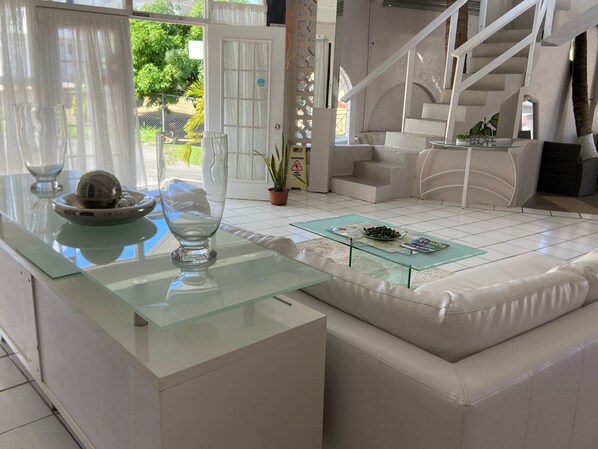 Una sala de estar moderna con una mesa de centro de vidrio, un sofá blanco y una escalera.