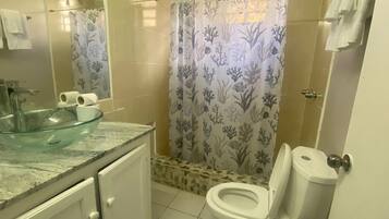Un baño con lavamanos de vidrio, un inodoro y una cortina de ducha con motivos marinos.