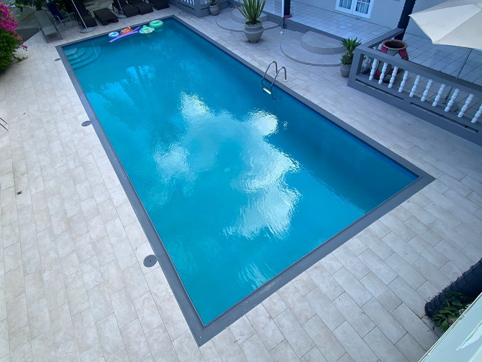 A rectangular swimming pool with a clear blue water surface, surrounded by light-colored tiled flooring.