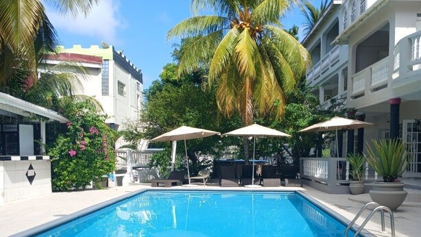 Una piscina con sillas de descanso y sombrillas, rodeada de palmeras y edificios.