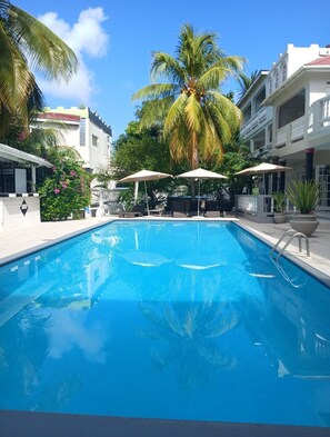 A swimming pool with lounge chairs and umbrellas, surrounded by palm trees and buildings. - Bay Heights Escape- Courtyard Studios (Gros Islet)