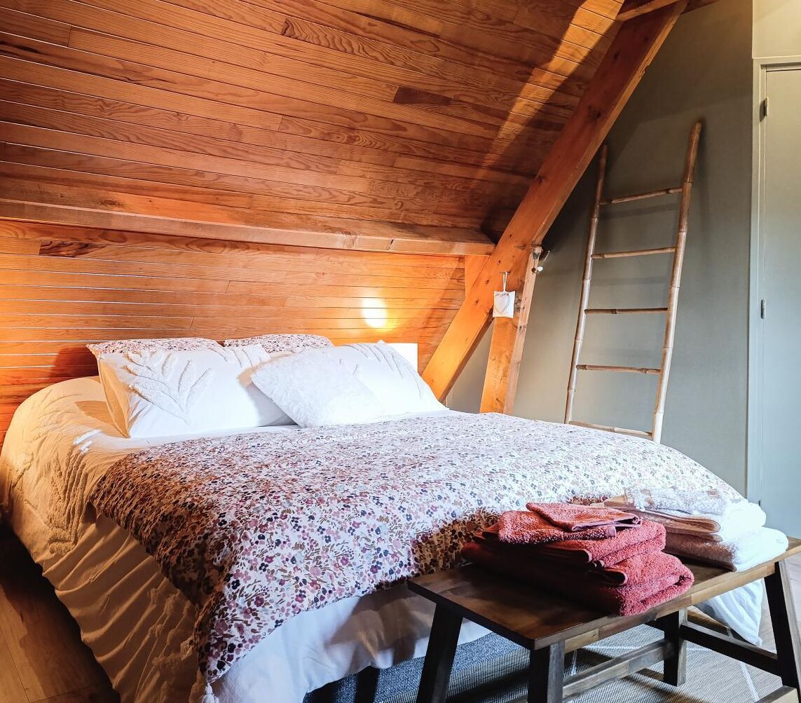 Ein Schlafzimmer mit Holzboden, einem Bett mit weißer und floraler Bettwäsche und einer Holzleiter an der Wand.