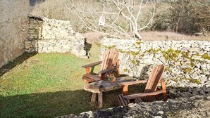 Un espace extérieur rustique aménagé avec deux chaises en bois et une table, entouré de murs en pierre et d’une pelouse verdoyante.