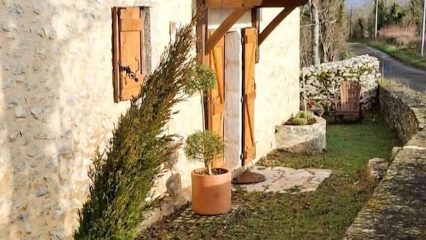Un bâtiment rustique avec un toit en pente, une véranda en bois et un mur en pierre.