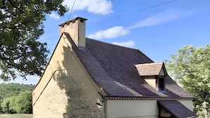 Une maison de campagne en pierre, avec un toit en pente, une cheminée et un petit porche agrémenté d’un pot de fleurs.