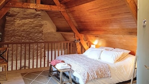Une chambre confortable située dans les combles, avec un plafond en bois, un mur en pierre et un lit recouvert d’une couvre-lit à motifs floraux.