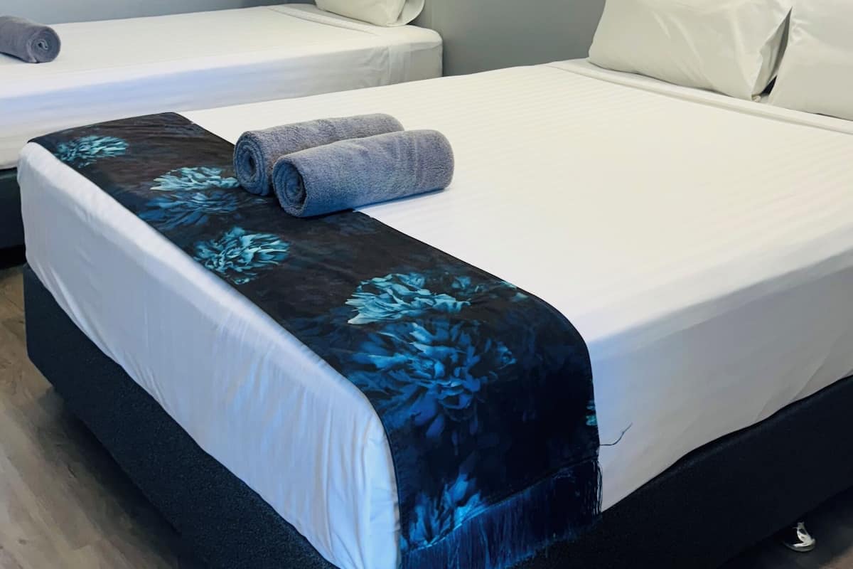 Habitación de hotel con dos camas, cada una con ropa blanca y una colcha de flores azules. Hay dos lámparas de pared sobre cada cama.