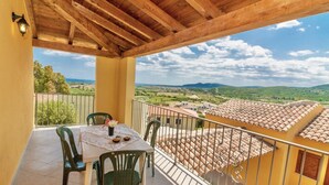 A balcony with a table and chairs, overlooking a scenic landscape with buildings and hills.