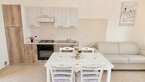 A compact kitchen with a gas stove, oven, and white cabinets. A dining table with chairs is positioned in front of the kitchen.