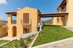 A yellow building with a balcony, a well-maintained lawn, and a clear blue sky.