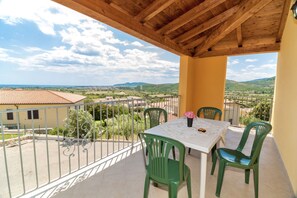 A balcony with a table and chairs, a view of the countryside, and a wooden ceiling.