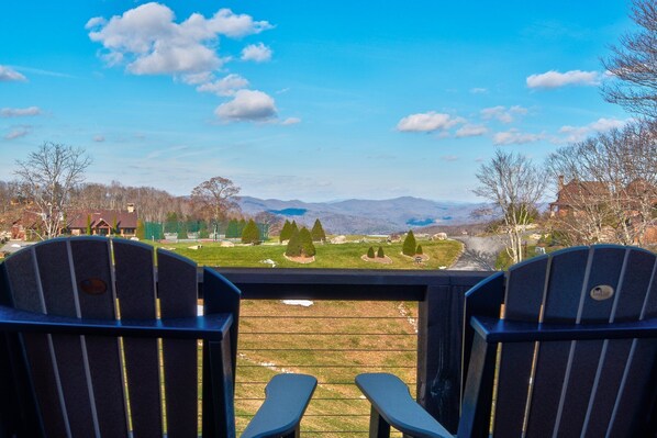 Two Adirondack chairs facing a scenic view of a park with mountains in the distance.
