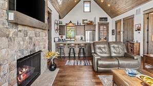A cozy living room with a stone fireplace, leather sofa, and a wooden dining area. - Sommer Hus at Eagles Nest: Pet Friendly Single Level (Banner Elk)