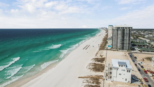 A coastal hotel with a beach view, a parking area, and a road leading to the beach. - Comfortable Emerald Coast Retreat! Only 3 minute walk to the white sandy BEACH! (Panama City Beach)