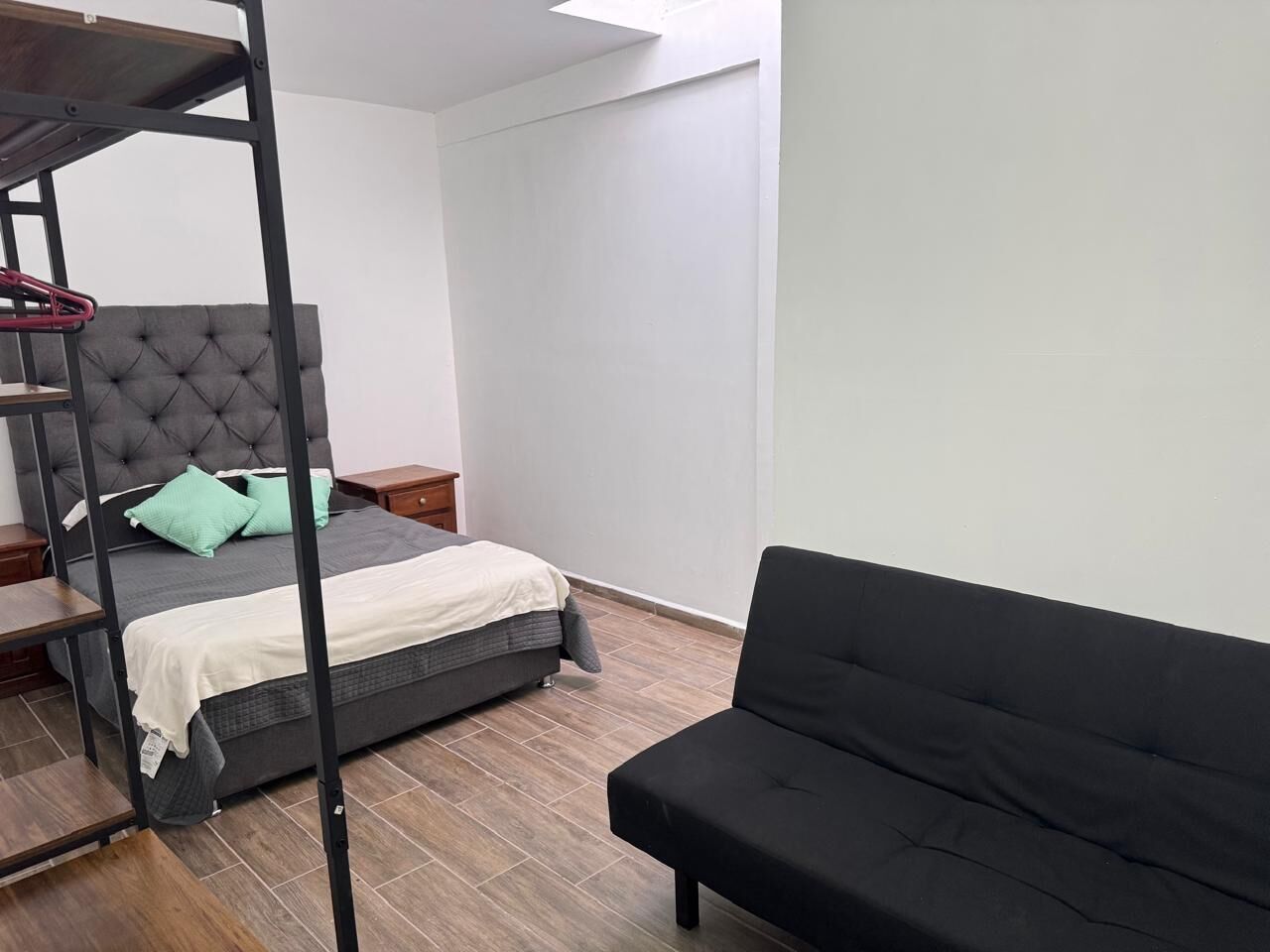 Ein Schlafzimmer mit einem Bett, einer schwarzen Couch, einem hölzernen Nachttisch und einem grauen, gepolsterten Kopfteil.