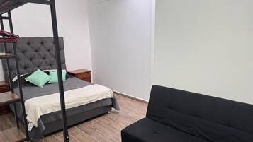 Ein Schlafzimmer mit einem Bett, einer schwarzen Couch, einem hölzernen Nachttisch und einem grauen, gepolsterten Kopfteil.