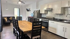 A modern kitchen with white cabinets, a wooden dining table, and a black sofa in the adjacent living area. - Hermosa Province Duplex House (Large Groups) (Guadalajara)