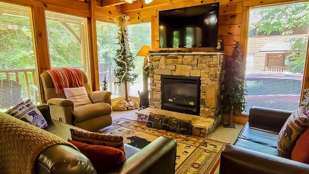 A cozy living room with a stone fireplace, leather sofas, and large windows.