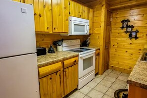 A kitchen with wooden cabinets, a white refrigerator, a microwave, a stove, and a sink. - Cozy Cabin w Game Room hot tub Creek (Gatlinburg)