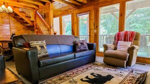 A cozy living room with a black leather sofa, a patterned throw blanket, and a chair with a red and white striped throw.