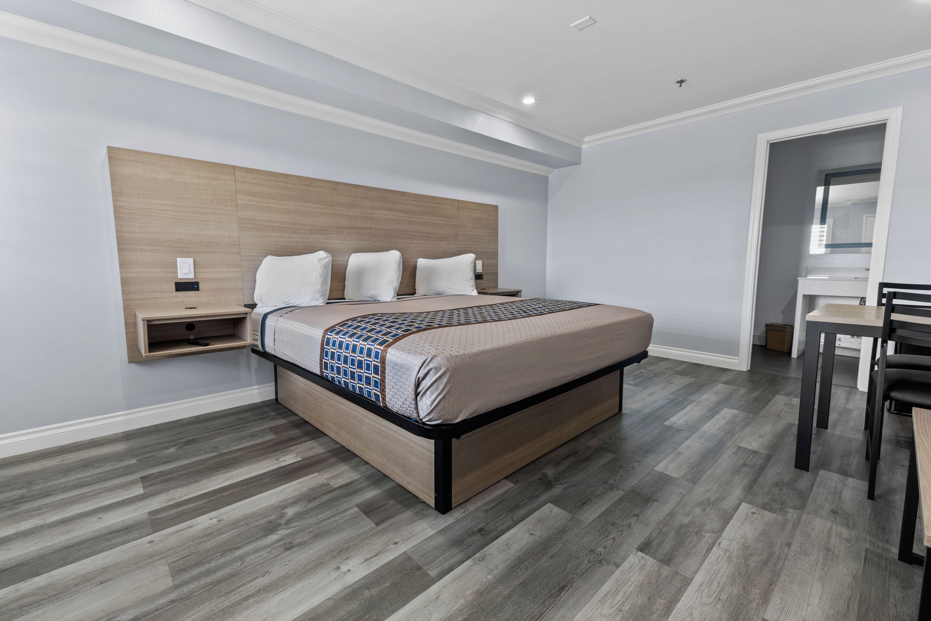 A modern hotel room with a bed, bedside table, and a small desk with a chair.
