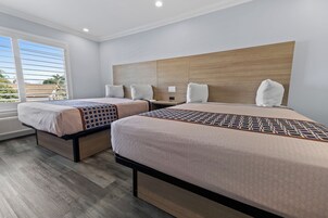 Quarto de hotel com duas camas, cabeceira de madeira e uma janela grande com persianas.