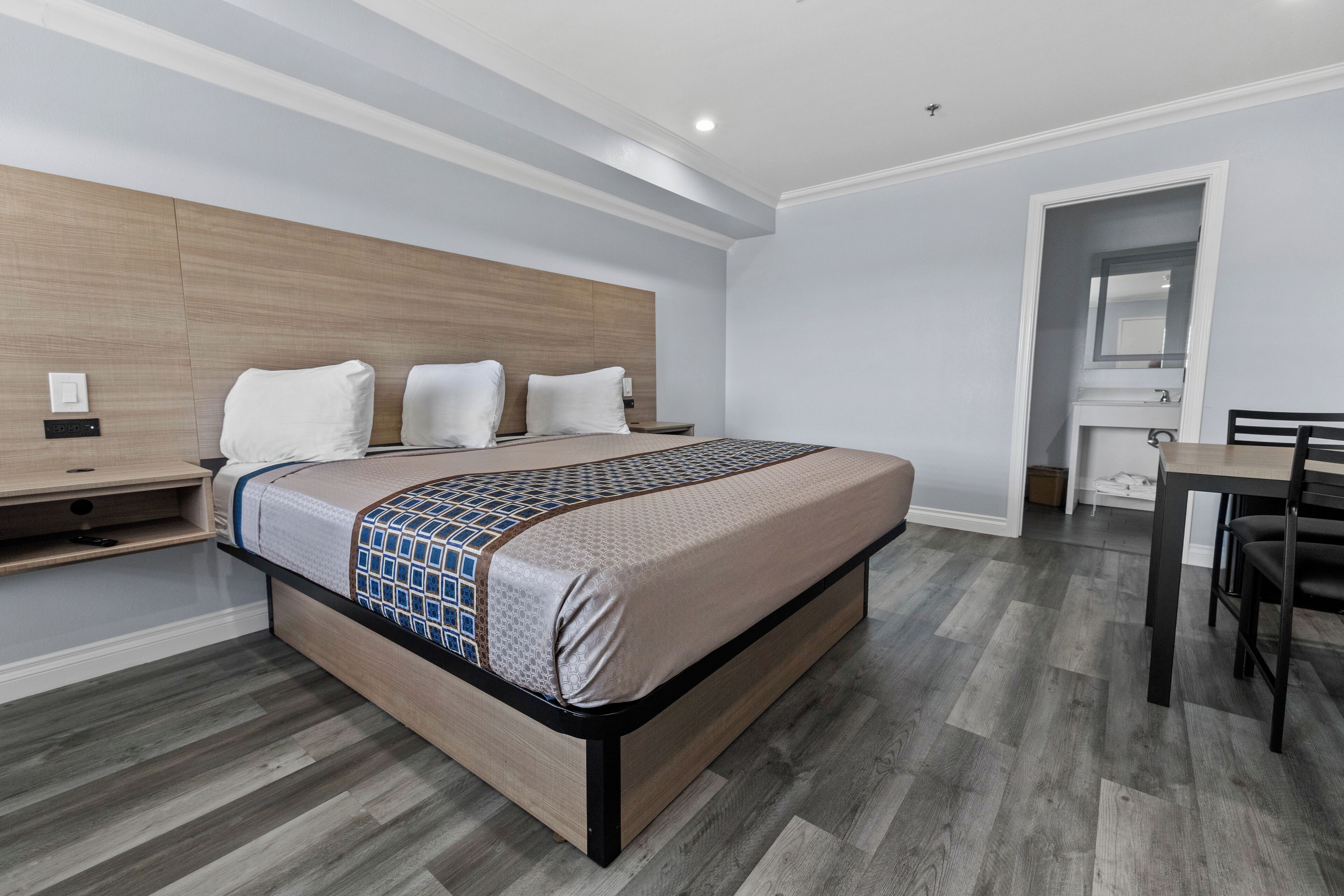 A modern bedroom with a wooden headboard, a large bed with a patterned bedspread, a bedside table, and a desk with a chair.