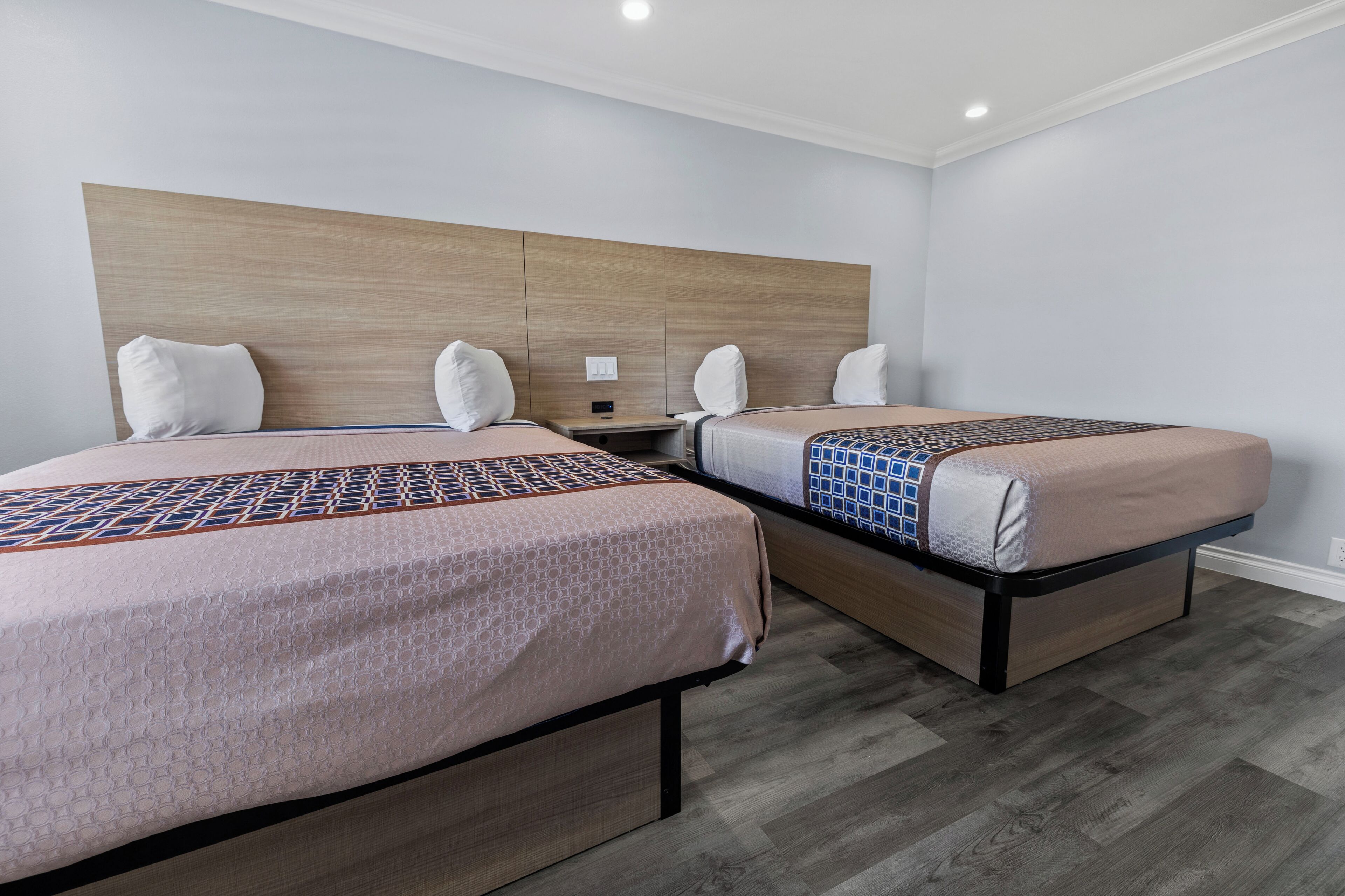 Una camera d'albergo con due letti, una testiera in legno e un comodino.