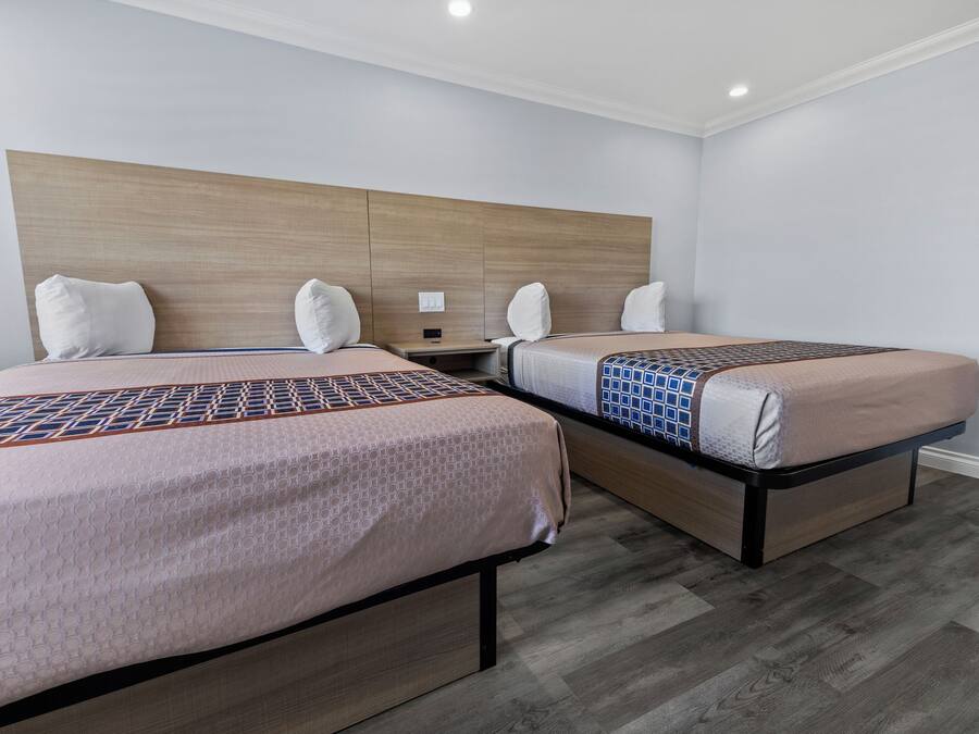 Una camera d'albergo con due letti, una testiera in legno e un comodino.