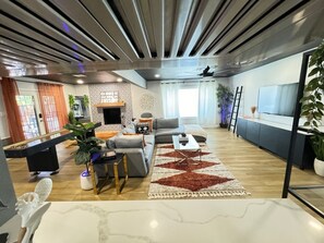 A modern living room with a grey sofa, a coffee table, and a patterned rug. There is a fireplace, a TV, and a plant in the room.