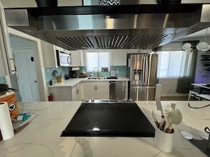 A modern kitchen with a black induction cooktop, stainless steel appliances, and a white marble countertop.