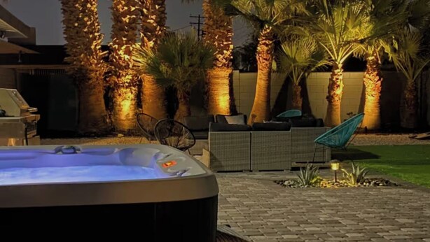 A hot tub in a backyard with palm trees and outdoor furniture. - Jacuzzi • Huge Yard • Sleeps 8-10 • Modern spacious layout • 5 minutes to strip (Las Vegas)