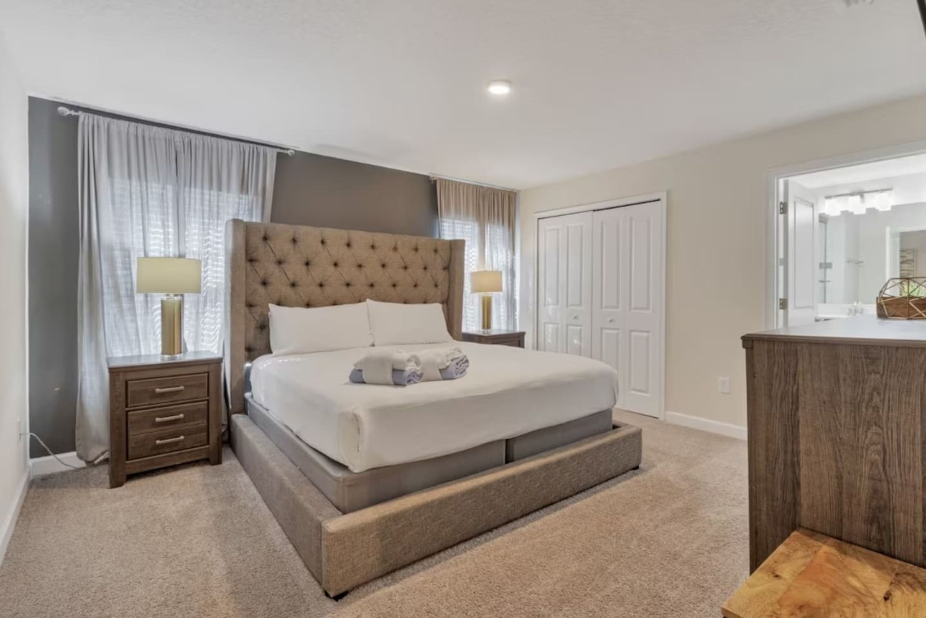 A bedroom with a large bed, a nightstand with a lamp, a wooden dresser, and a mirror.