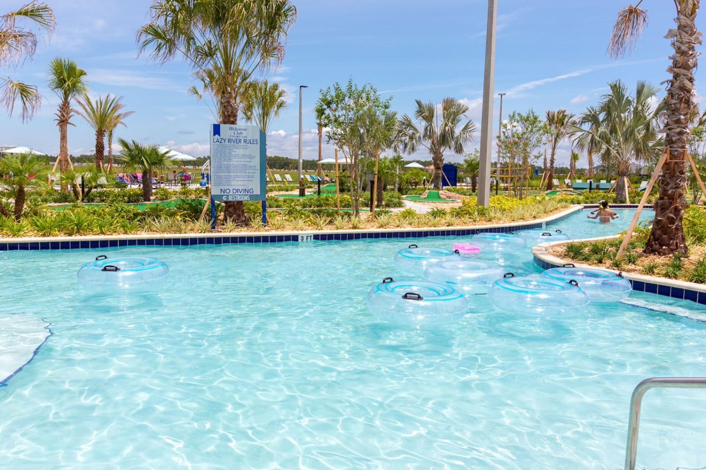 Ein Poolbereich mit klarem, blauem Wasser, umgeben von Palmen und einem Schild mit der Aufschrift 'Lazy River Rules'.