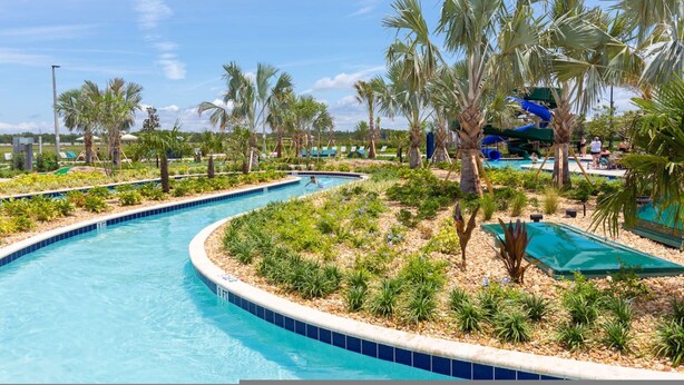 Zona de piscina con fuente acuática curva, palmeras y tobogán de agua.