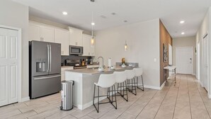 A modern kitchen with white cabinets, stainless steel appliances, and a central island with bar stools. - Your 5bdr House w Pool - 4959 (Kissimmee)