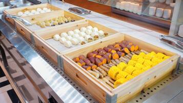 Un bufé con diversos alimentos en fuentes de madera, incluyendo maíz, batatas y albóndigas.
