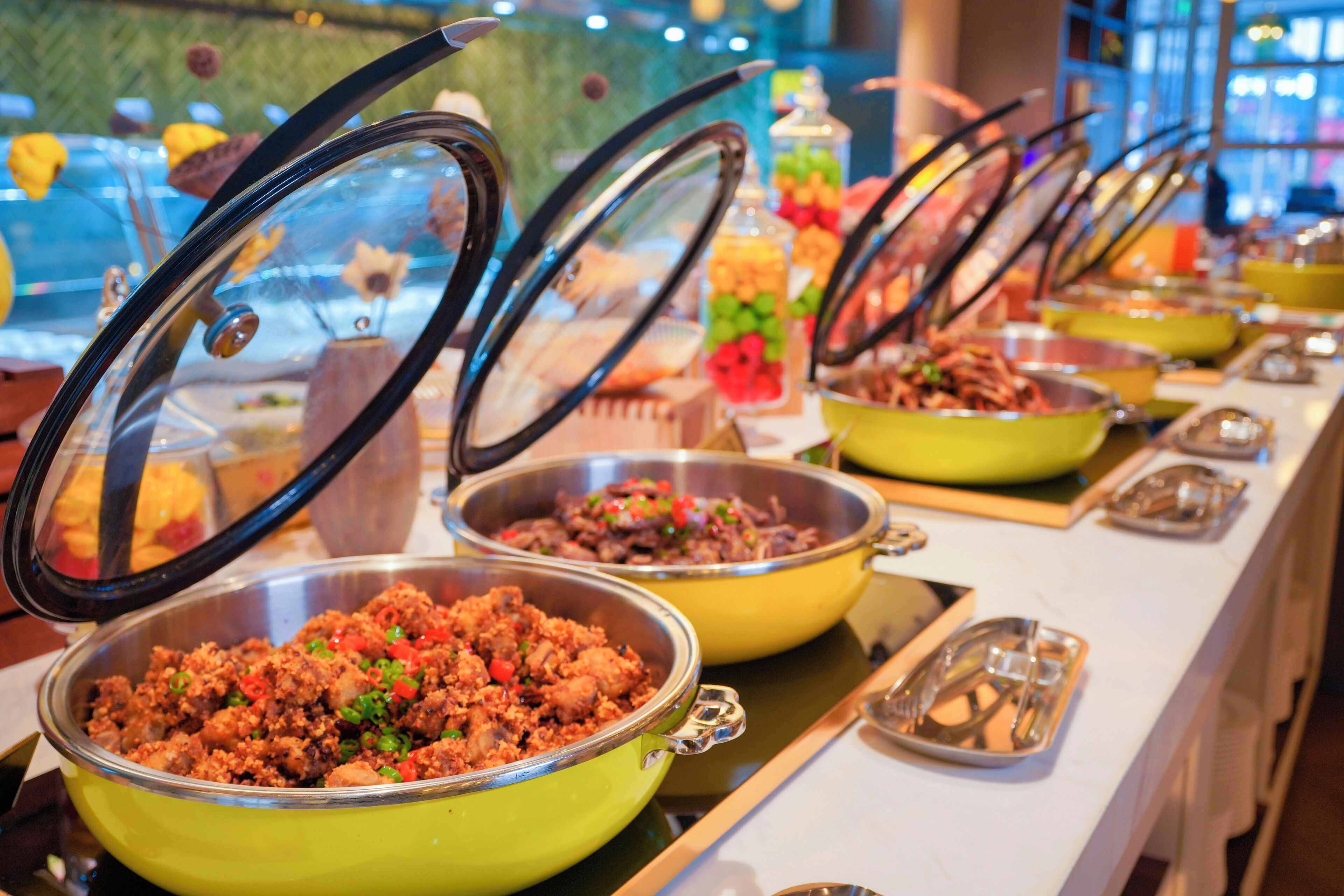 Een buffet met diverse gerechten in gele en zilveren schalen, waarvan sommige afgedekt zijn.