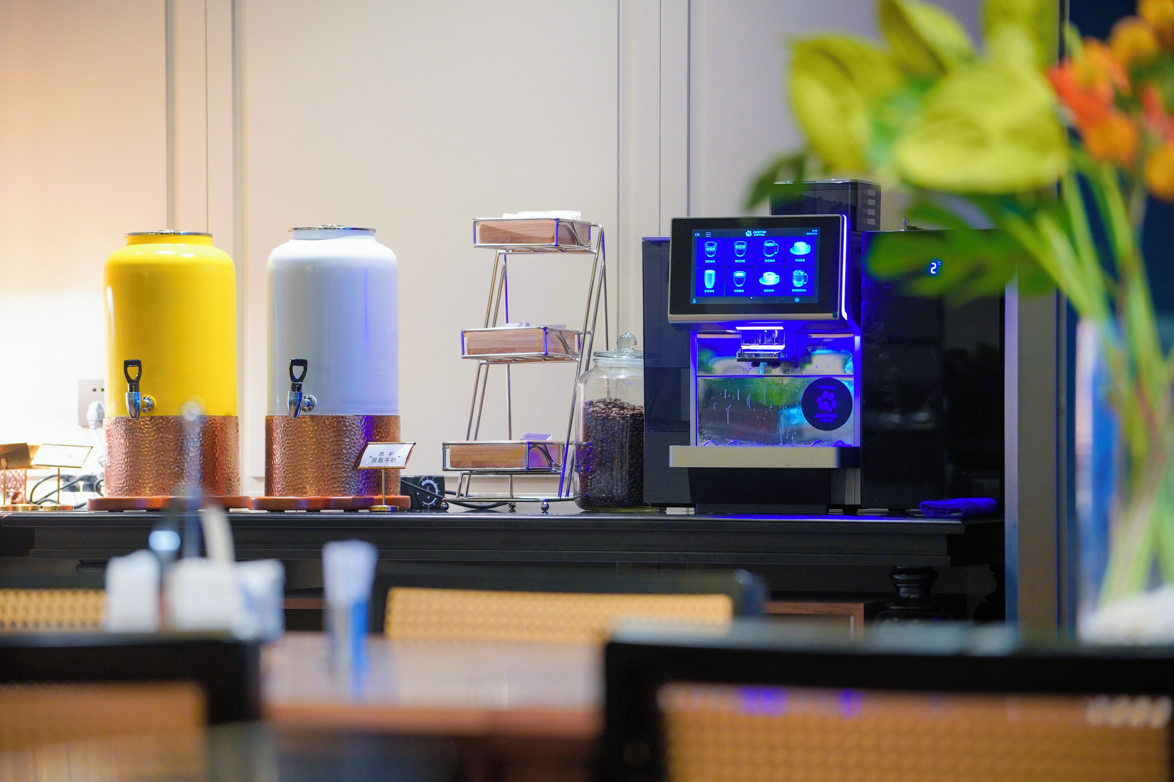 A bar area with a coffee machine, two large beverage dispensers, and a small display screen.